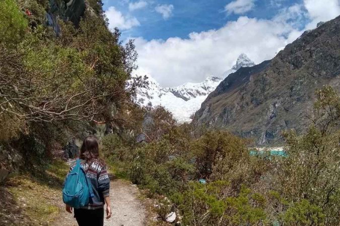 A woman hiking a mountain trail toward a snow-capped peak, one of the most scenic trekking destinations in Asia.