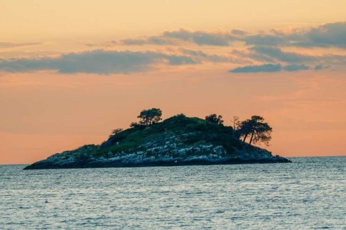 A small, rocky island silhouette at sunset, representing the ultimate perfect island escape.