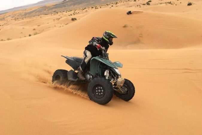 A person driving an ATV quad bike through sandy dunes during a multi day desert trek.